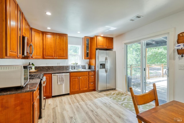 kitchen featuring dark stone countertops, sink, light wood-type flooring, and appliances with stainless steel finishes