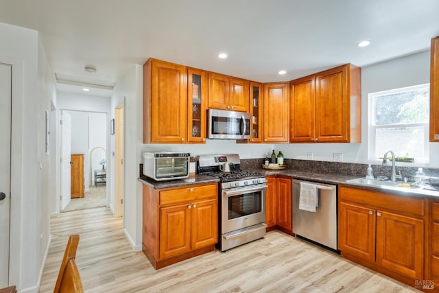 kitchen with stainless steel appliances, sink, dark stone countertops, and light hardwood / wood-style flooring