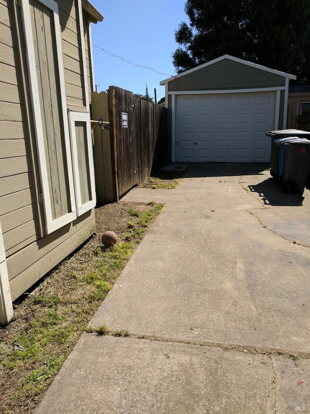 view of side of home featuring a detached garage, driveway, an outbuilding, and fence