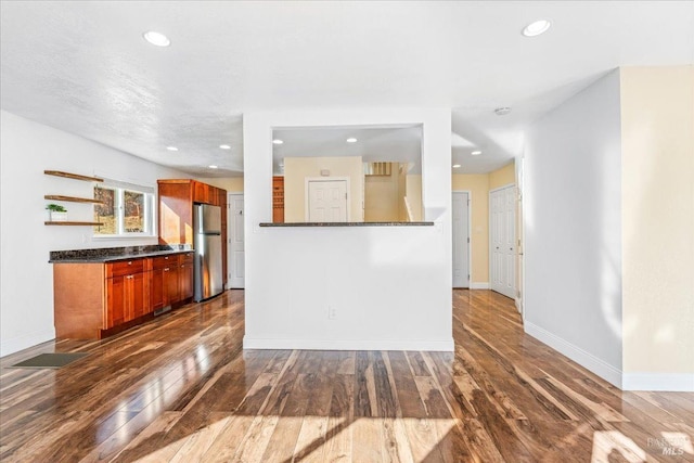 kitchen featuring dark stone countertops, stainless steel fridge, and dark wood-type flooring