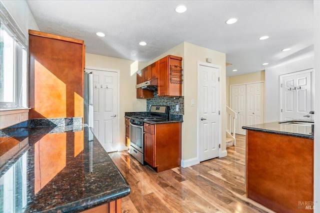 kitchen with light wood-type flooring, backsplash, dark stone counters, stainless steel appliances, and sink