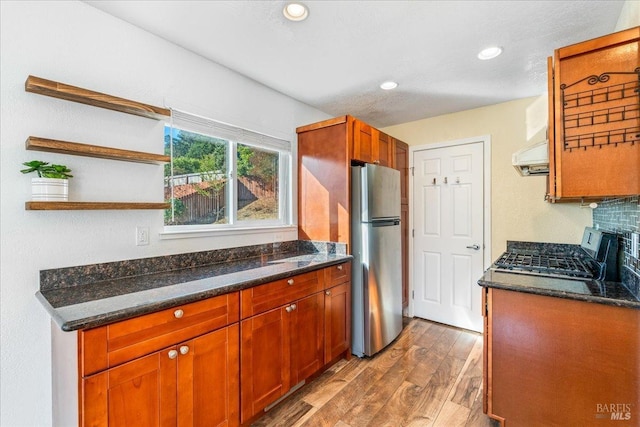 kitchen featuring stainless steel fridge, stove, ventilation hood, dark stone countertops, and hardwood / wood-style floors