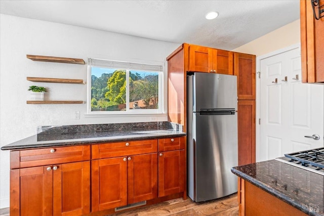 kitchen with stainless steel refrigerator, dark stone countertops, a textured ceiling, and light wood-type flooring