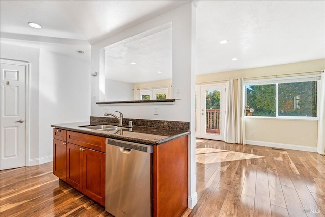 kitchen with sink, stainless steel dishwasher, dark stone countertops, wood-type flooring, and a textured ceiling