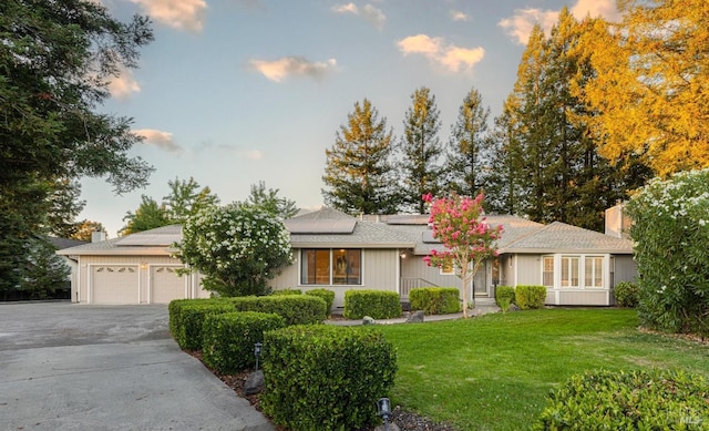 single story home featuring solar panels, a garage, and a yard