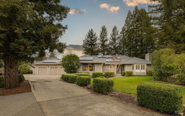 ranch-style home featuring a yard, a garage, and solar panels