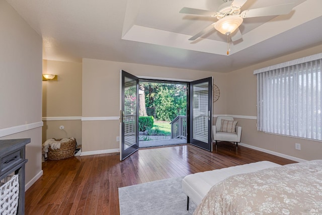 bedroom with wood-type flooring, access to outside, ceiling fan, and a tray ceiling