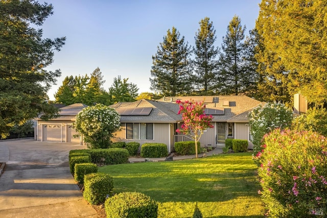 ranch-style house featuring a garage, a front lawn, and solar panels