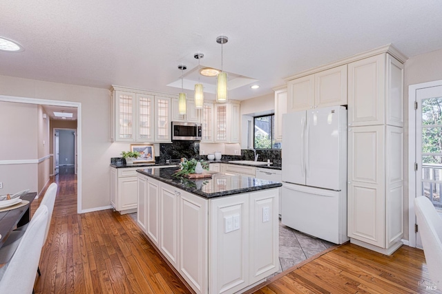 kitchen with sink, hanging light fixtures, white refrigerator, a kitchen island, and light wood-type flooring