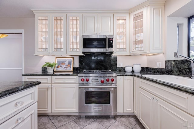 kitchen with appliances with stainless steel finishes, sink, dark stone countertops, white cabinets, and light tile patterned floors