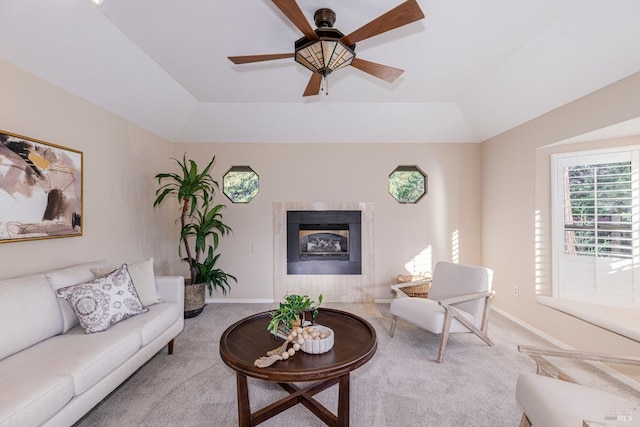 living room featuring vaulted ceiling, a tray ceiling, carpet flooring, ceiling fan, and a fireplace