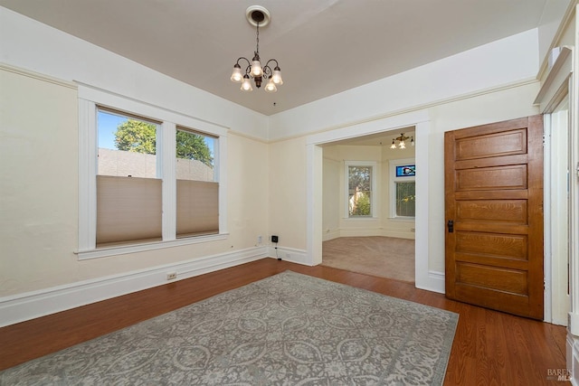 unfurnished room with an inviting chandelier and dark hardwood / wood-style flooring