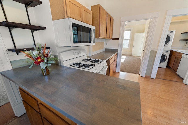 kitchen with stacked washing maching and dryer, white appliances, and light hardwood / wood-style flooring