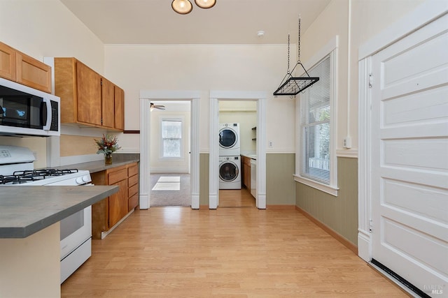 kitchen with stacked washer and dryer, decorative light fixtures, light hardwood / wood-style floors, and white gas range oven