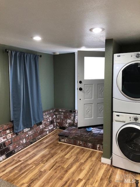 laundry area featuring wood-type flooring and stacked washer / dryer