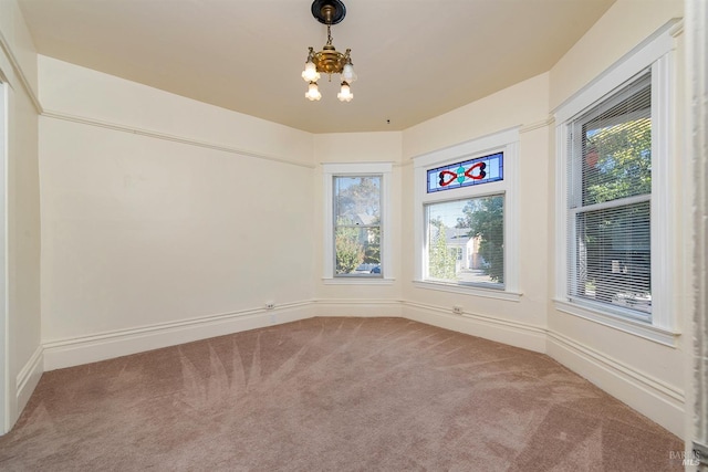 carpeted empty room with plenty of natural light and a chandelier