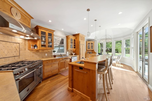 kitchen featuring pendant lighting, high end stainless steel range, a notable chandelier, light hardwood / wood-style floors, and decorative backsplash