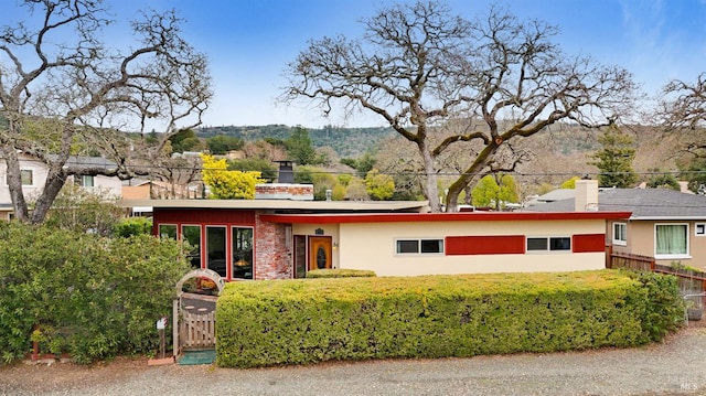 view of front of house featuring a chimney, a mountain view, fence, and stucco siding