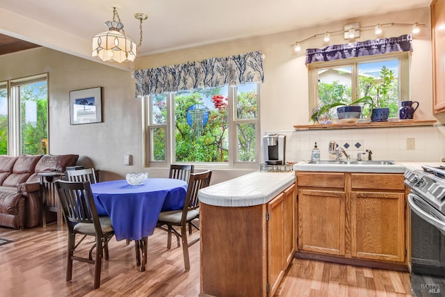 kitchen featuring stainless steel stove, a peninsula, light wood finished floors, brown cabinetry, and tasteful backsplash