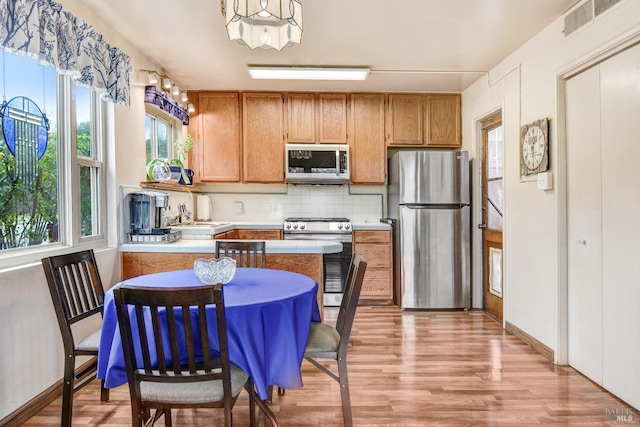 kitchen featuring stainless steel appliances, brown cabinetry, light countertops, and backsplash