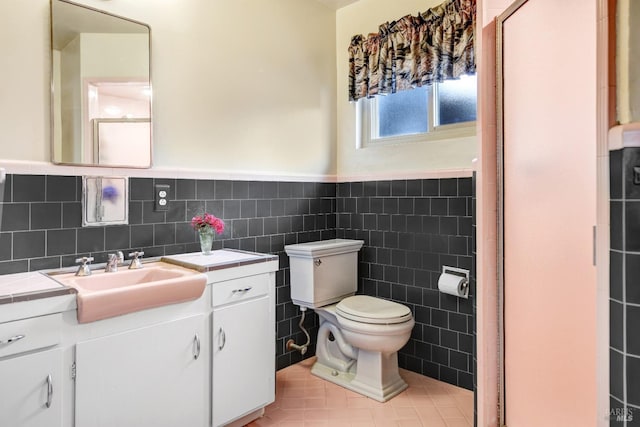 bathroom featuring vanity, tile patterned flooring, a wainscoted wall, toilet, and tile walls