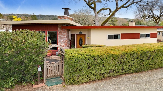 view of front facade with a chimney, stucco siding, and a gate