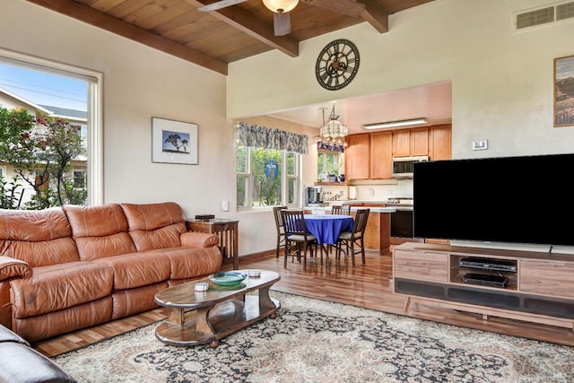 living room featuring light wood-type flooring, visible vents, beamed ceiling, ceiling fan with notable chandelier, and wooden ceiling