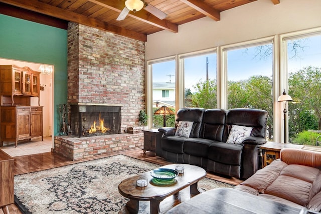 living area with beam ceiling, a fireplace, wooden ceiling, and a ceiling fan