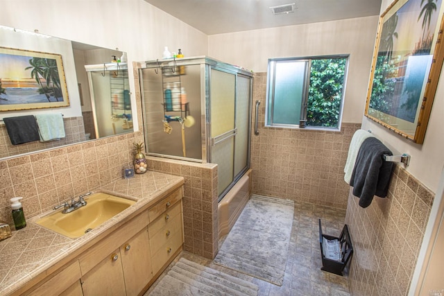 bathroom with tile walls, enclosed tub / shower combo, and vanity