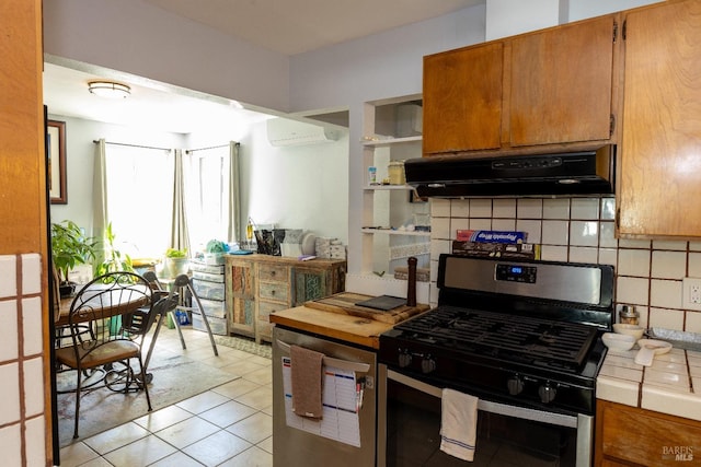 kitchen featuring tile counters, light tile patterned flooring, decorative backsplash, gas range, and a wall mounted air conditioner