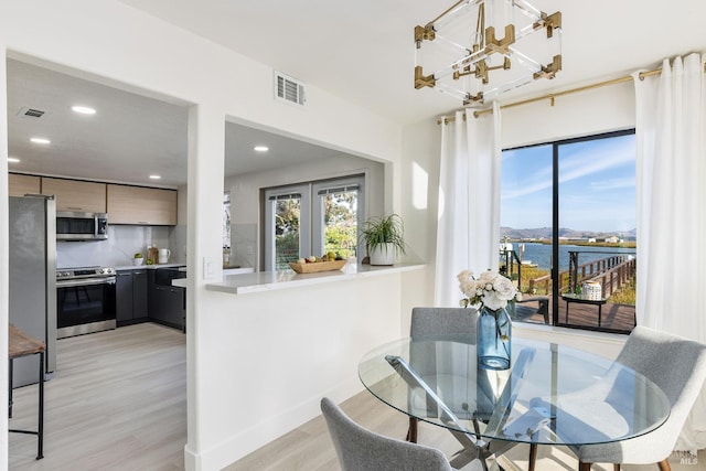 dining area with a chandelier, light hardwood / wood-style floors, and a water view