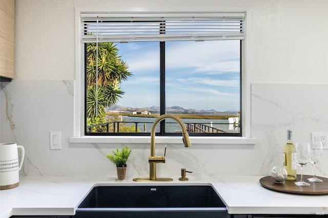 interior details with light stone countertops, a water view, and sink