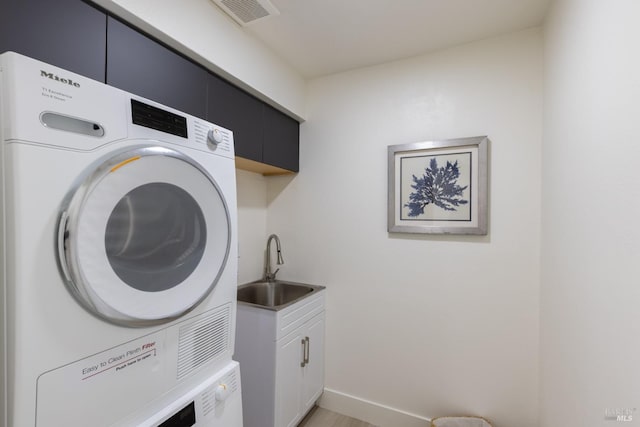 clothes washing area featuring cabinets, stacked washer / drying machine, and sink