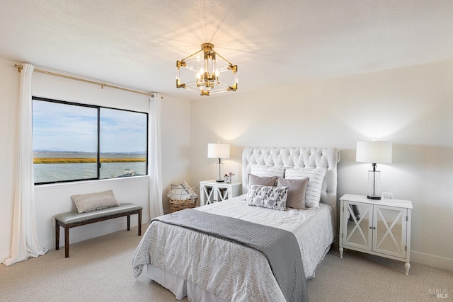 bedroom with a textured ceiling, a water view, carpet flooring, and an inviting chandelier