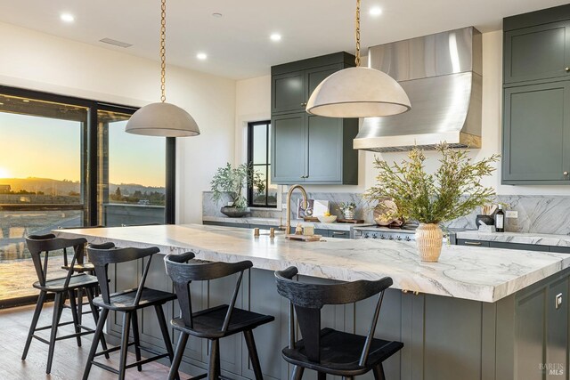 kitchen with light stone counters, decorative light fixtures, wall chimney exhaust hood, and tasteful backsplash