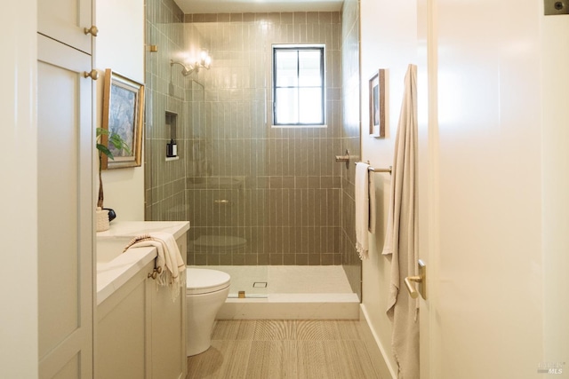 bathroom featuring a tile shower, tile patterned floors, vanity, and toilet