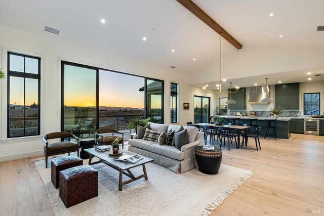 living room with light wood-type flooring, beamed ceiling, a notable chandelier, beverage cooler, and high vaulted ceiling