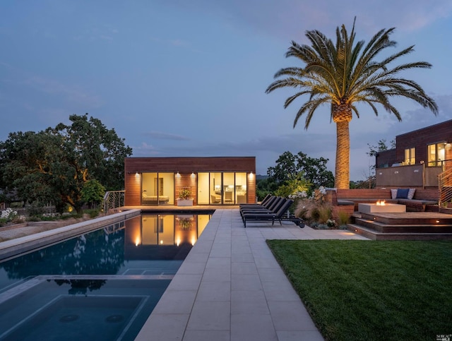 back house at dusk featuring a pool with hot tub, a lawn, and a patio area