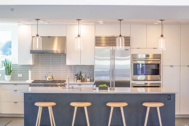 kitchen with wall chimney exhaust hood, white cabinets, appliances with stainless steel finishes, and pendant lighting