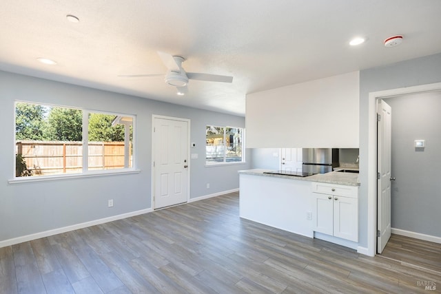 kitchen with light stone counters, white cabinets, ceiling fan, stainless steel fridge, and light hardwood / wood-style flooring