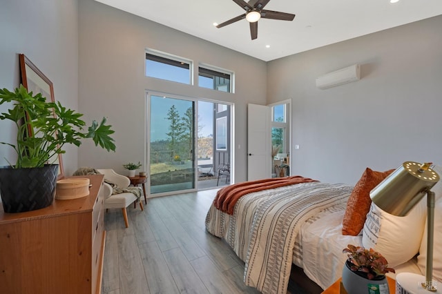 bedroom featuring a towering ceiling, a ceiling fan, access to exterior, a wall mounted AC, and light wood-type flooring