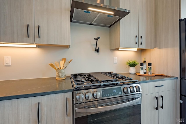 kitchen featuring range hood, modern cabinets, freestanding refrigerator, and stainless steel gas range oven