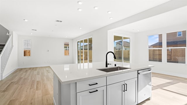 kitchen featuring an island with sink, dishwasher, sink, and light wood-type flooring