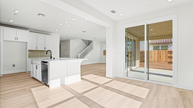 kitchen with sink, light hardwood / wood-style flooring, an island with sink, and white cabinets