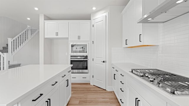 kitchen with white cabinetry, appliances with stainless steel finishes, light wood-type flooring, and exhaust hood