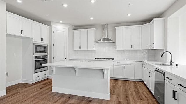 kitchen featuring sink, white cabinetry, black appliances, a kitchen island, and wall chimney range hood