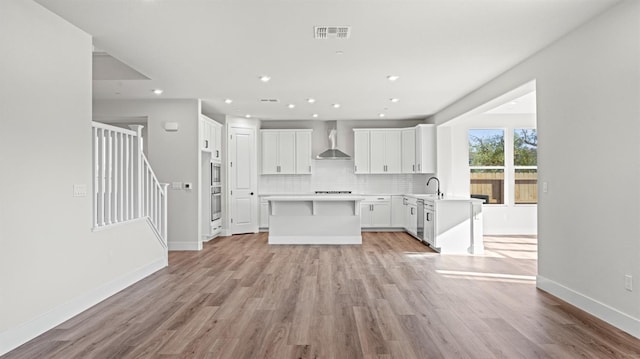 kitchen with wall chimney range hood, sink, light hardwood / wood-style floors, white cabinets, and decorative backsplash