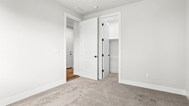 unfurnished bedroom with light carpet and a walk in closet