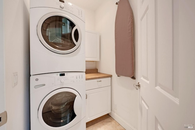 clothes washing area featuring baseboards, cabinet space, and stacked washer and dryer