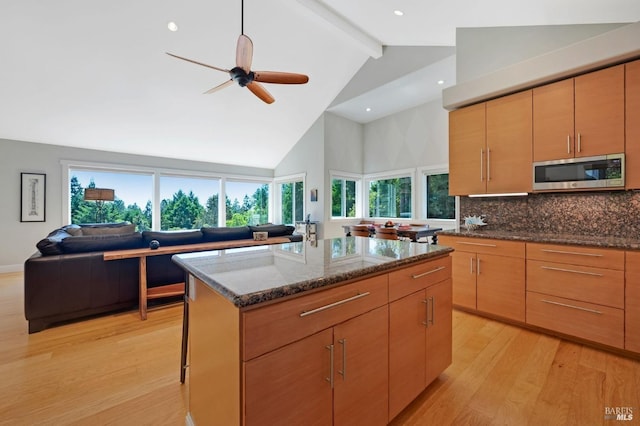 kitchen featuring stainless steel microwave, a kitchen island, beamed ceiling, open floor plan, and dark stone counters